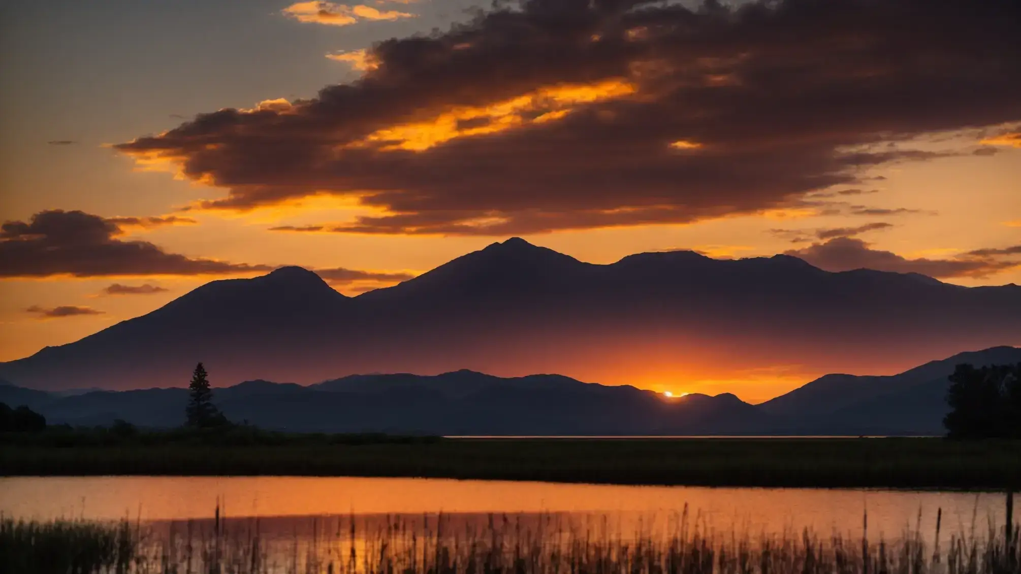 a vibrant sunset casts a warm golden glow over a tranquil lake, where the still water reflects the colorful sky and the silhouette of majestic mountains in the background.