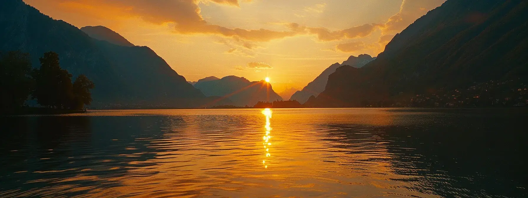 a breathtaking sunset casts golden hues across a serene lake, with silhouetted mountains framing the horizon and soft ripples reflecting the vibrant colors of the sky.