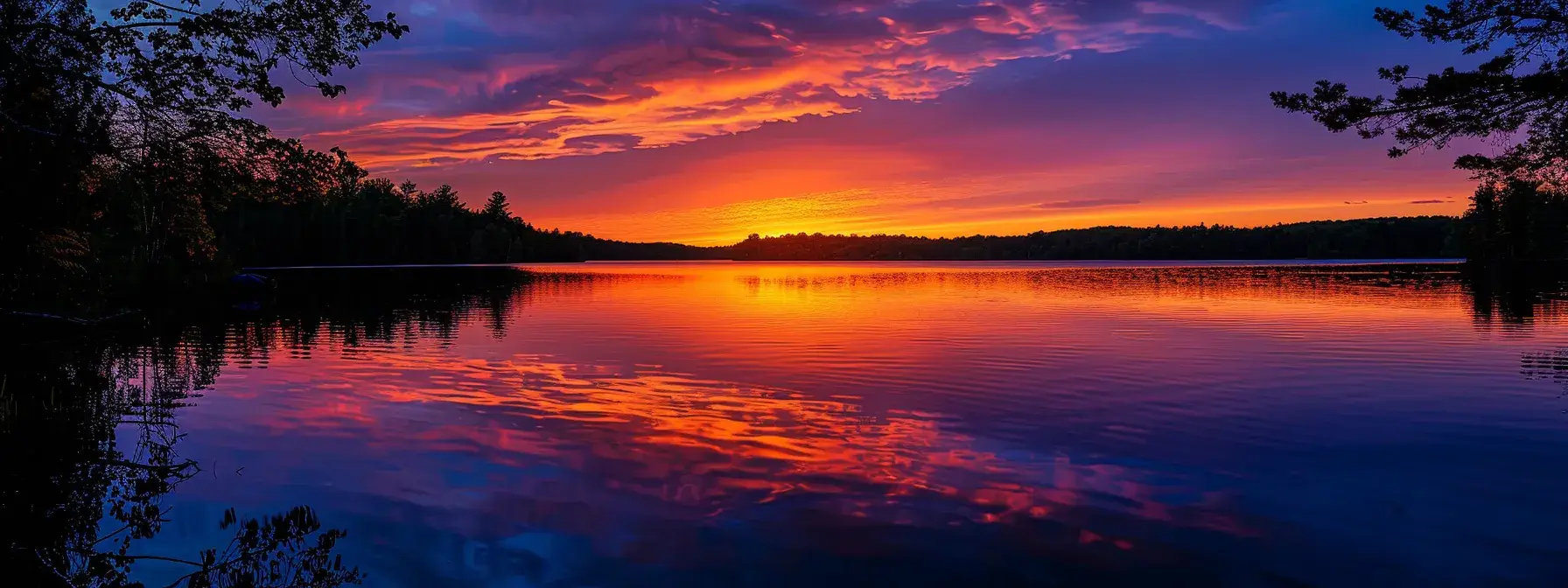 a breathtaking sunset casts vivid hues of orange and pink across a serene lake, reflecting the colorful sky while silhouetted trees frame the tranquil waters.