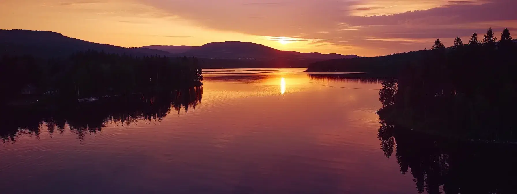 a vibrant sunset casts a warm glow over a tranquil lake, with reflections of deep oranges and purples mirrored on the water's surface, surrounded by silhouetted trees against a clear horizon.