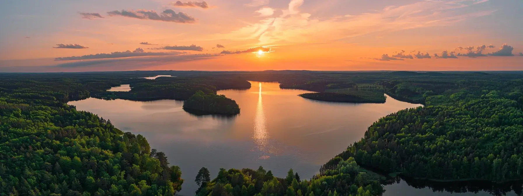 a vibrant sunset over a tranquil lake reflects fiery shades of orange and pink, surrounded by lush green forests under a clear sky.